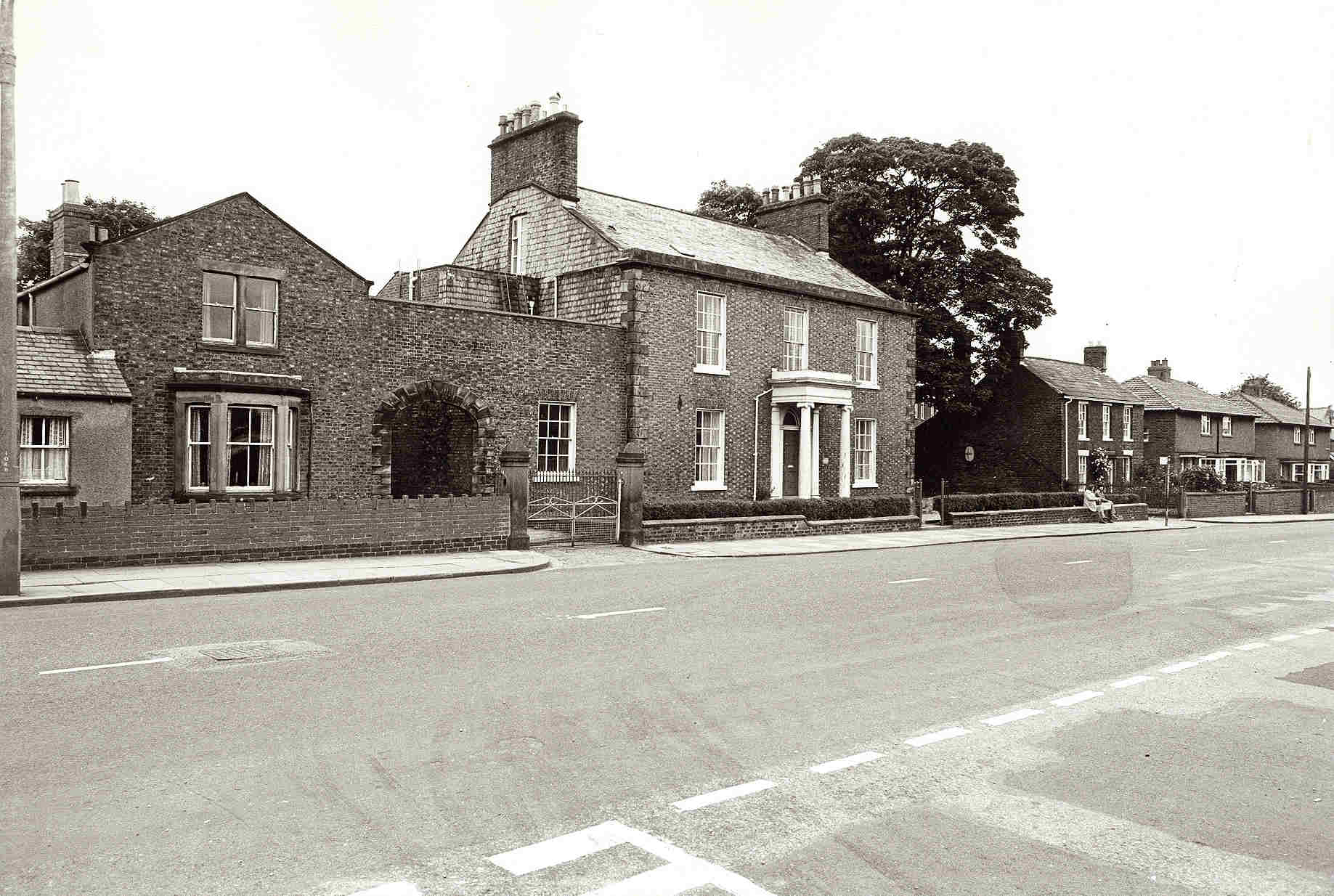 A black-and-white photograph of Coledale Hall, a Georgian brick building set back from a wide road