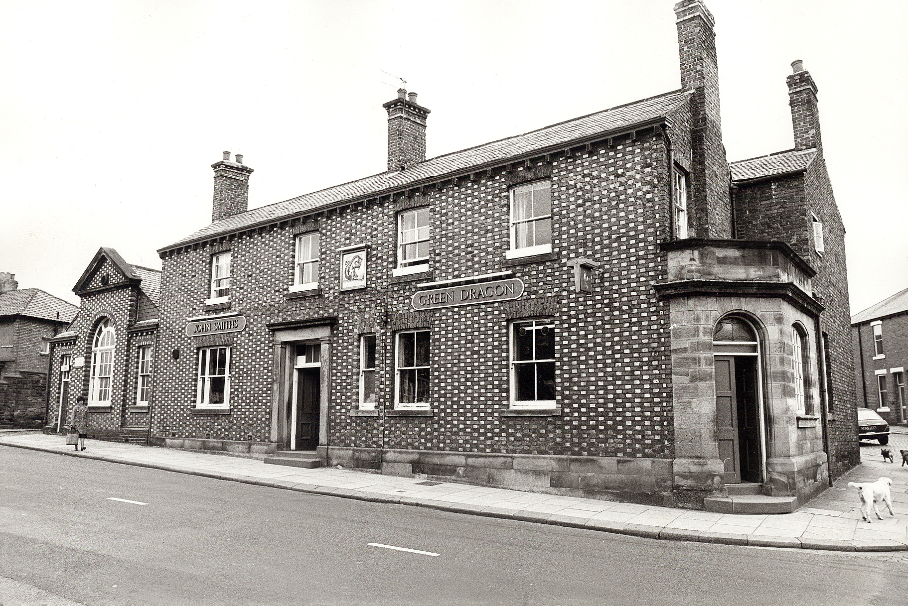 A black-and-white photograph of the Green Dragon Inn, a Victorian brick corner pub with a John Smith's sign