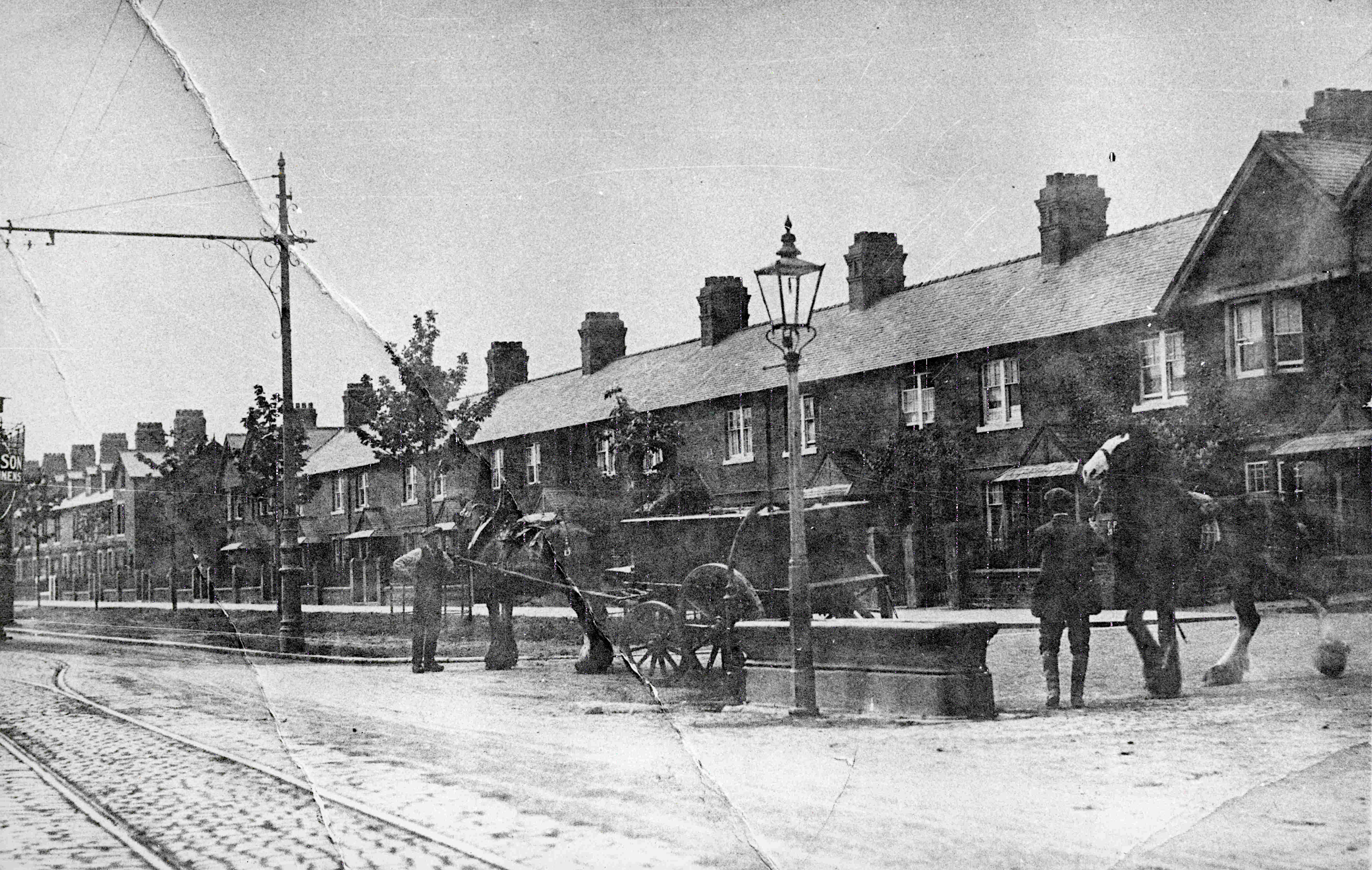 A black-and-white photograph of horse-drawn vehicles on a cobbled Carlisle street, with tram tracks visible and terraced housing behind