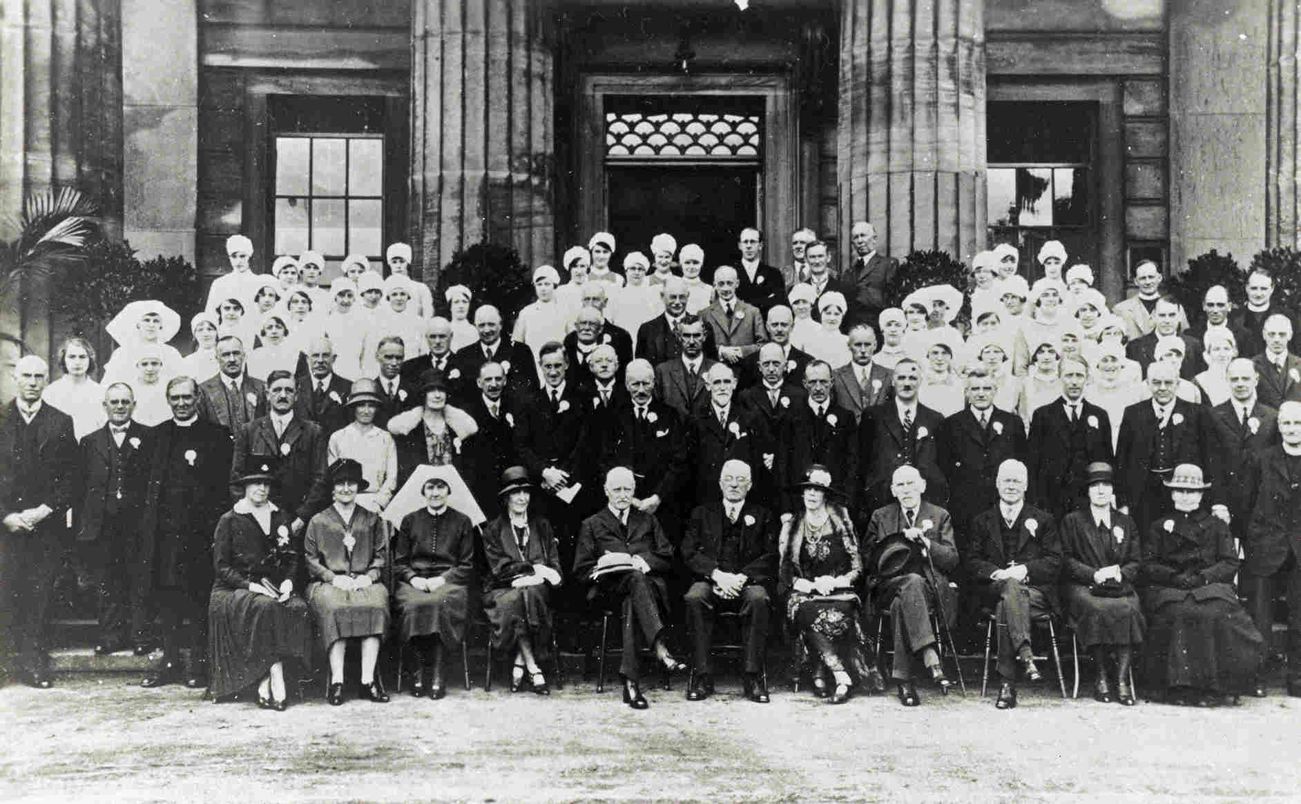 A formal group photograph of doctors and nurses on the infirmary steps — rows of nurses in white caps and doctors in dark suits