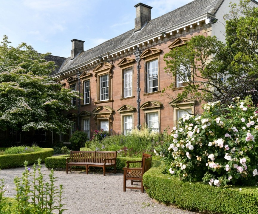 The original Tullie House building seen from its walled garden, with roses in bloom on a sunny day